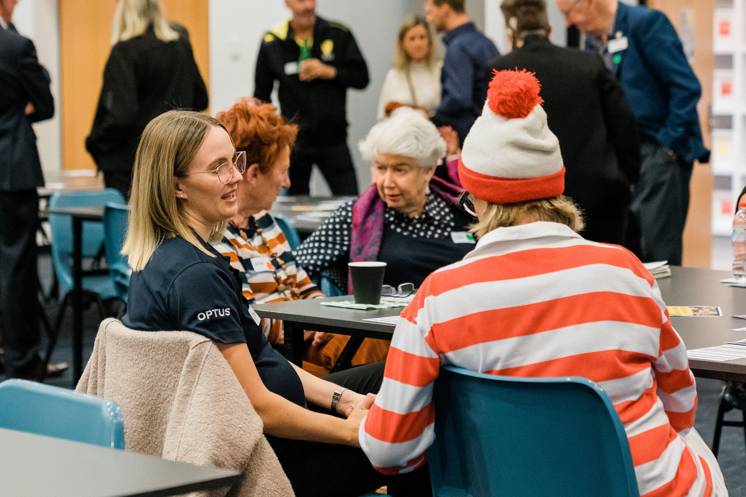 Group of women sitting around a table chatting, one dressed as Where's Wally