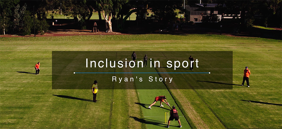 Aerial view of a group of people playing cricket on a grassy field. They are wearing yellow and orange T-shirts with dark colored shorts or pants. There is a text overlay on the image reading “ Inclusion in sport - Ryan’s Story”.