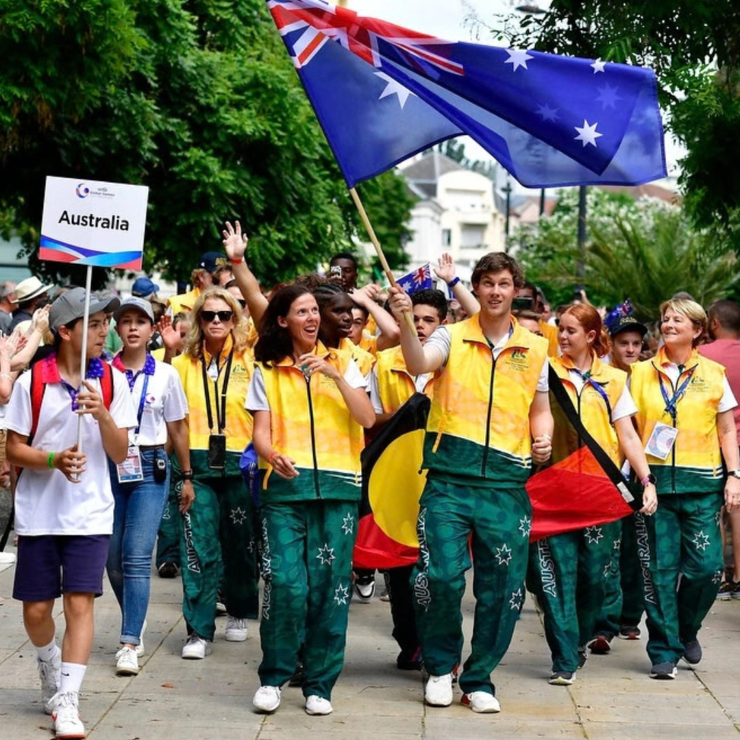 Australian sports team walking down the street dressed in yellow and green sports clothes. They are holding the Australian flag.